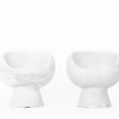 Deux fauteuils en ciment blanc, créations iconiques de Willy Guhl, semblent flotter sur fond blanc.