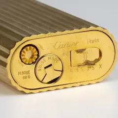 Gros plan sur le fond d'un briquet Cartier plaqué or, gravé "Swiss Made" et un numéro de série. Une pièce de collection pour une estimation.