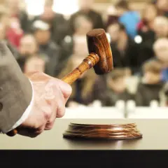 Un commissaire-priseur tient un maillet, prêt à frapper le bloc. La foule attend, espérant acquérir un objet convoité, peut-être au-delà du prix de réserve enchère.
