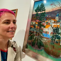 Une femme aux cheveux roses admire un tableau d'Étienne Cournault représentant un village pittoresque sous un ciel coloré.