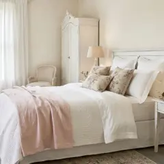 Chambre douillette au style shabby chic, avec un lit blanc, des coussins fleuris, une armoire ancienne et des rideaux légers.