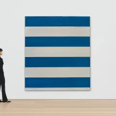 Une femme observe une œuvre de Michel Parmentier, une grande toile rayée de bleu et de blanc, dans une galerie d'art.