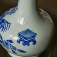 Gros plan sur un vase chinois ancien, blanc avec des motifs bleus de fleurs et de symboles.