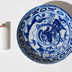 Assiette chinoise ancienne signature, décorée de motifs bleus sur fond blanc, avec un briquet à côté pour l'échelle.