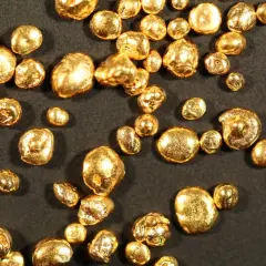 Grains d'or brillant, certains ressemblant à des pépites, d'autres à des billes. Chaque pièce, un petit trésor de 24 carats, scintille sur fond sombre.