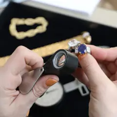 Maintenant, où faire expertiser des bijoux gratuitement ? Une main examine une bague saphir et diamant avec une loupe.