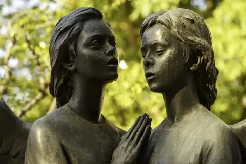Deux visages d'anges en bronze se font face. Leurs mains jointes aident à comment reconnaître du bronze, patiné par le temps.