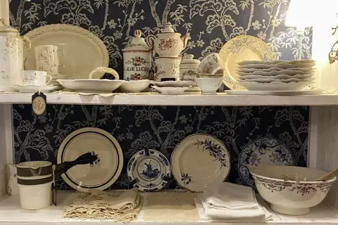Étagères remplies de vaisselle ancienne, dont des tasses, des assiettes et des bols, avec un motif floral bleu sur fond sombre. Une étiquette mentionne "Porcelaine de Paris signature".