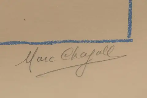 Signature manuscrite de Marc Chagall, artiste de renom, sur un fond beige avec des lignes bleues.