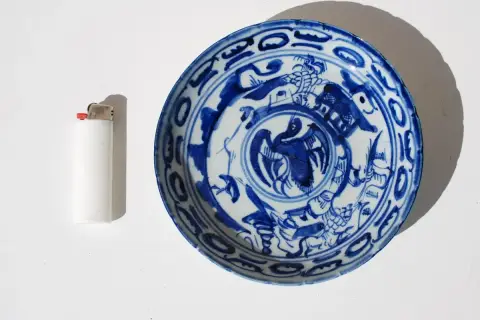Assiette chinoise ancienne signature, décorée de motifs bleus sur fond blanc, avec un briquet à côté pour l'échelle.