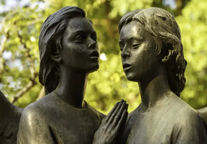 Deux visages d'anges en bronze se font face. Leurs mains jointes aident à comment reconnaître du bronze, patiné par le temps.