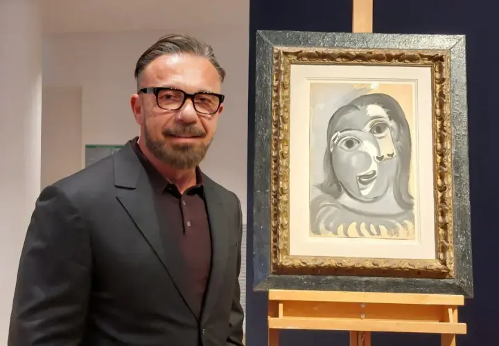 Un homme en costume pose à côté d'un tableau de Picasso, une œuvre qui pourrait bien battre des records de prix.