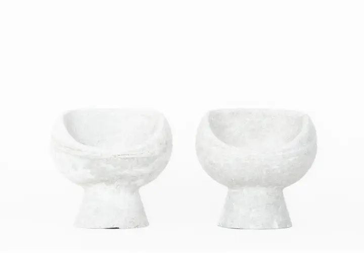 Deux fauteuils en ciment blanc, créations iconiques de Willy Guhl, semblent flotter sur fond blanc.