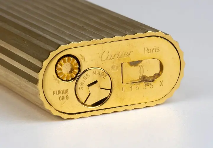 Gros plan sur le fond d'un briquet Cartier plaqué or, gravé "Swiss Made" et un numéro de série. Une pièce de collection pour une estimation.