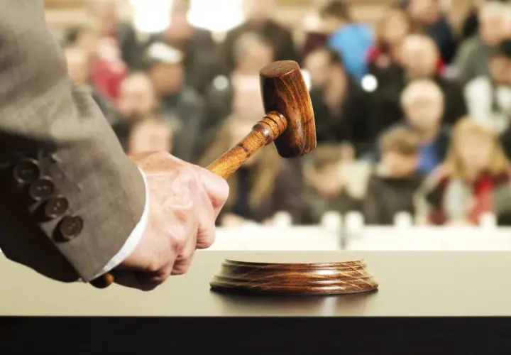 Un commissaire-priseur tient un maillet, prêt à frapper le bloc. La foule attend, espérant acquérir un objet convoité, peut-être au-delà du prix de réserve enchère.