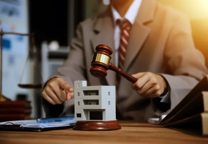 Un juge frappe avec son maillet sur une maquette de bâtiment, symbolisant une vente aux enchères immobilière.