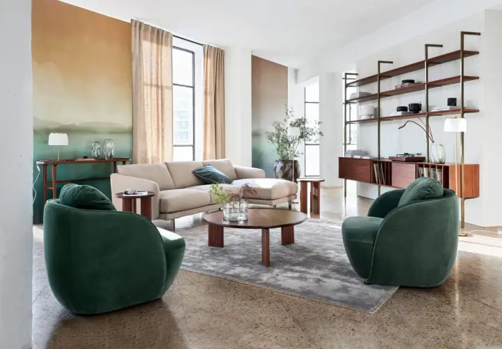 Salon moderne avec canapé beige, fauteuils verts et étagères en bois, ambiance mid century.