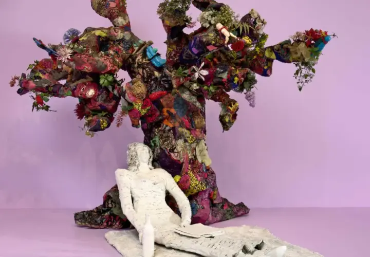 Sculpture d'arbre colorée et texturée, évoquant l'esprit de Niki de Saint Phalle. Une figure blanche repose à ses pieds.