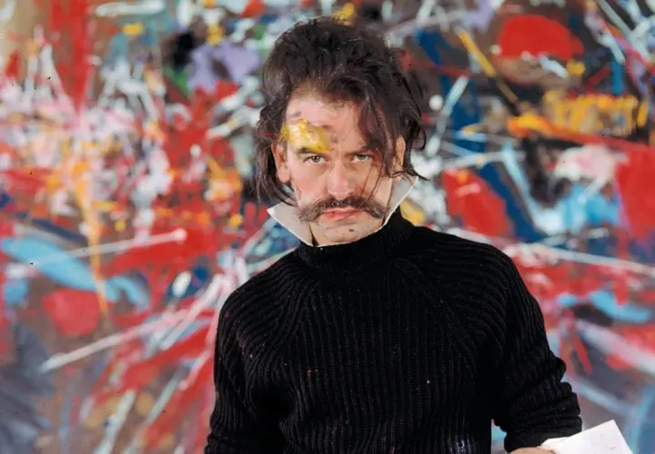 Georges Mathieu, lauréat du prix, pose devant une toile abstraite vibrante, son visage marqué par la peinture.