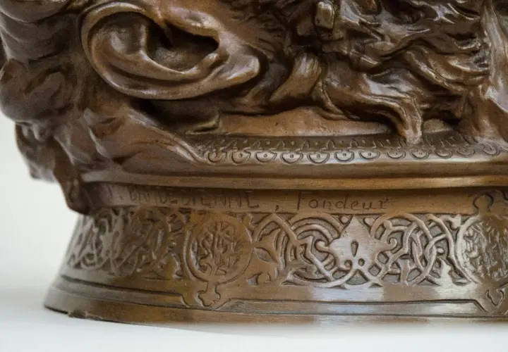 Détail d'une sculpture en bronze creux ou plein, ornée de motifs complexes et d'une inscription gravée.