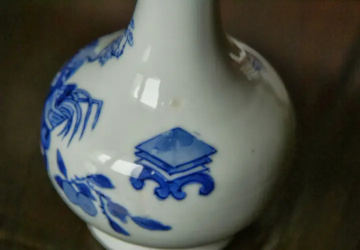 Gros plan sur un vase chinois ancien, blanc avec des motifs bleus de fleurs et de symboles.