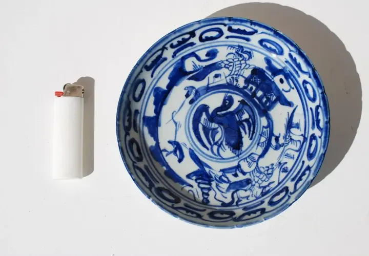 Assiette chinoise ancienne signature, décorée de motifs bleus sur fond blanc, avec un briquet à côté pour l'échelle.