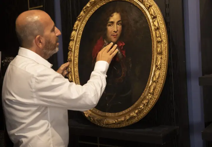 Un homme examine un portrait ancien. Il touche le cadre doré, peut-être pour comment estimer un tableau avec signature.