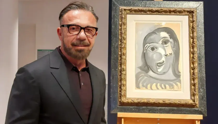 Un homme en costume pose à côté d'un tableau de Picasso, une œuvre qui pourrait bien battre des records de prix.