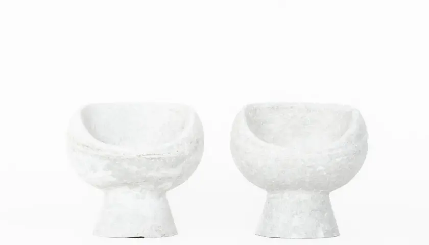 Deux fauteuils en ciment blanc, créations iconiques de Willy Guhl, semblent flotter sur fond blanc.