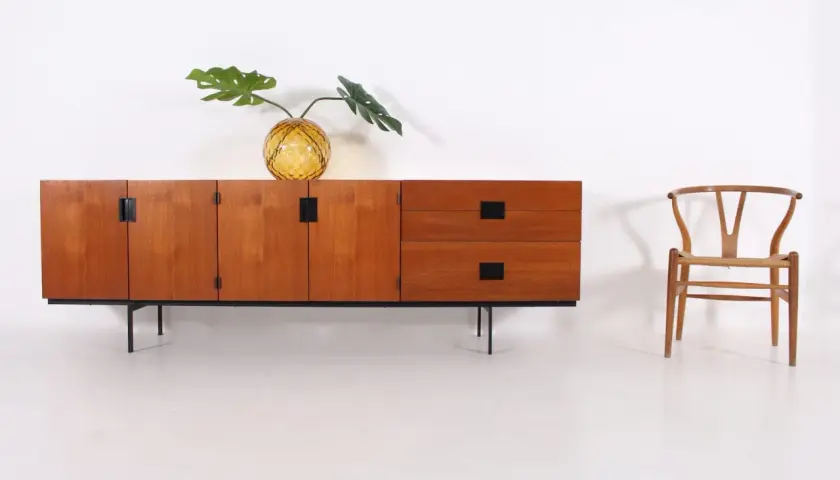 Buffet en teck par Cees Braakman, avec un vase en verre texturé et une feuille de Monstera. Une chaise Wishbone est placée à droite.
