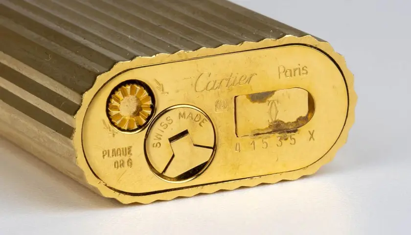 Gros plan sur le fond d'un briquet Cartier plaqué or, gravé "Swiss Made" et un numéro de série. Une pièce de collection pour une estimation.