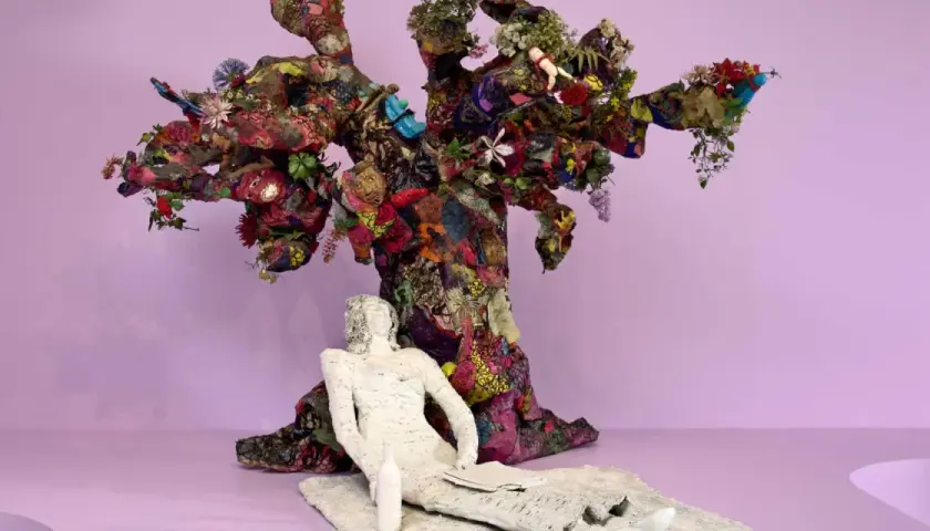 Sculpture d'arbre colorée et texturée, évoquant l'esprit de Niki de Saint Phalle. Une figure blanche repose à ses pieds.