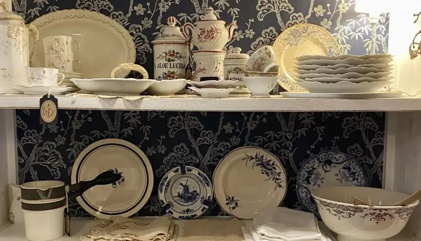 Étagères remplies de vaisselle ancienne, dont des tasses, des assiettes et des bols, avec un motif floral bleu sur fond sombre. Une étiquette mentionne "Porcelaine de Paris signature".