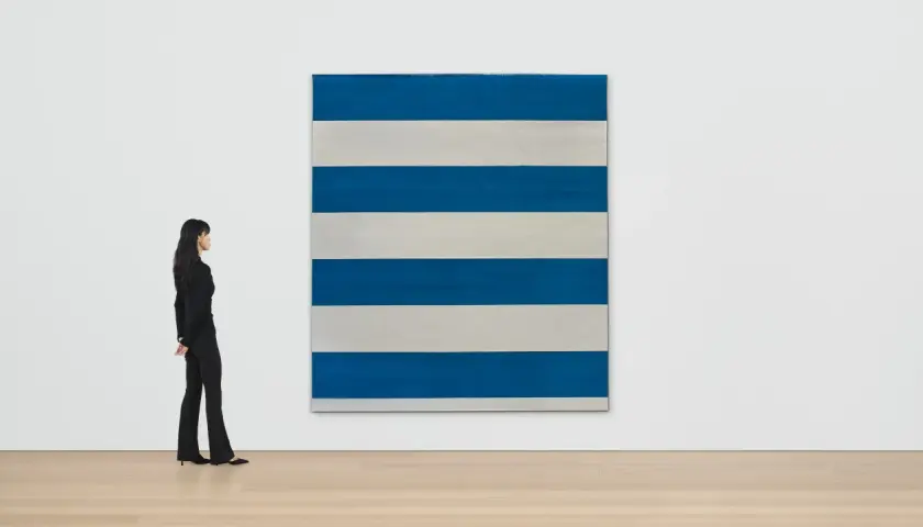 Une femme observe une œuvre de Michel Parmentier, une grande toile rayée de bleu et de blanc, dans une galerie d'art.