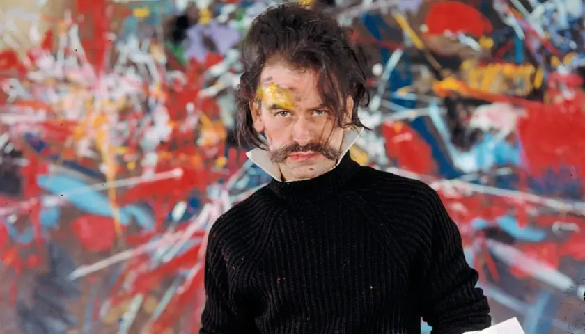 Georges Mathieu, lauréat du prix, pose devant une toile abstraite vibrante, son visage marqué par la peinture.