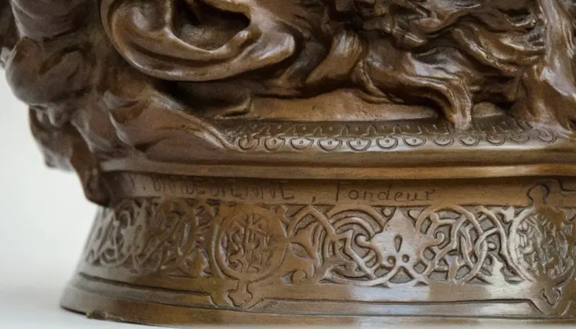 Détail d'une sculpture en bronze creux ou plein, ornée de motifs complexes et d'une inscription gravée.