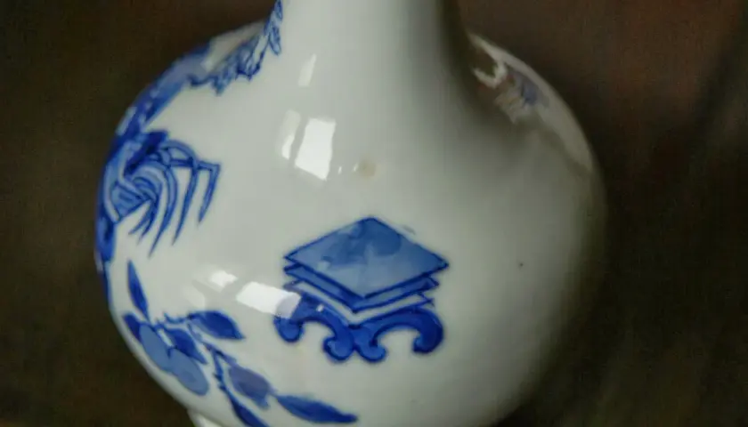 Gros plan sur un vase chinois ancien, blanc avec des motifs bleus de fleurs et de symboles.