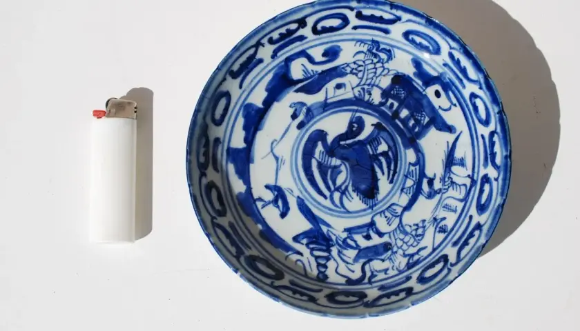 Assiette chinoise ancienne signature, décorée de motifs bleus sur fond blanc, avec un briquet à côté pour l'échelle.
