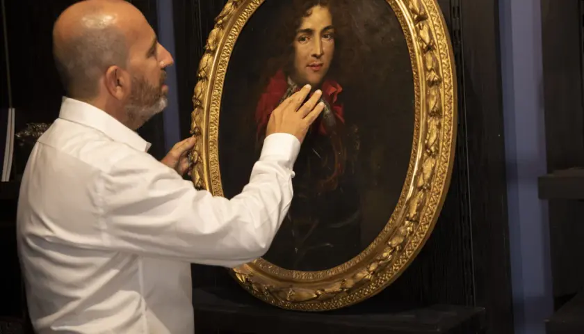 Un homme examine un portrait ancien. Il touche le cadre doré, peut-être pour comment estimer un tableau avec signature.