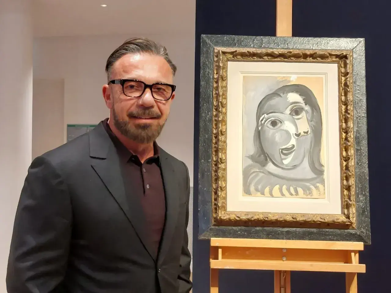 Un homme en costume pose à côté d'un tableau de Picasso, une œuvre qui pourrait bien battre des records de prix.