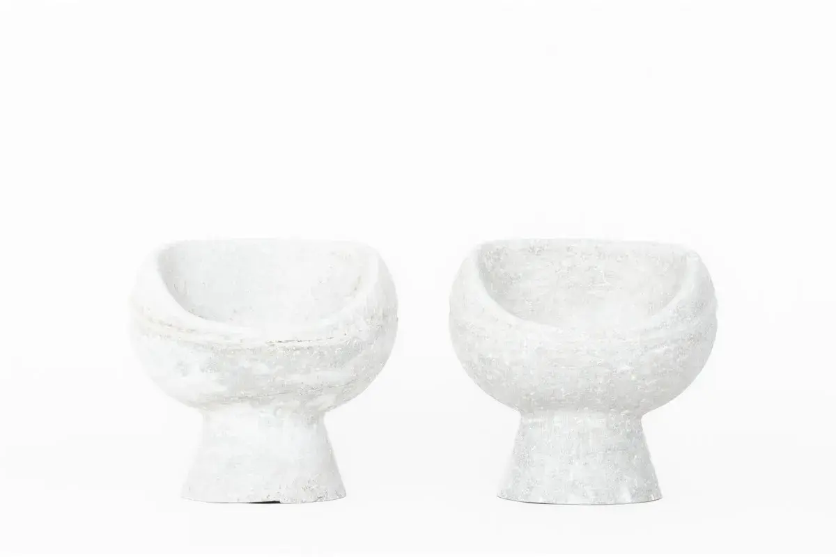Deux fauteuils en ciment blanc, créations iconiques de Willy Guhl, semblent flotter sur fond blanc.
