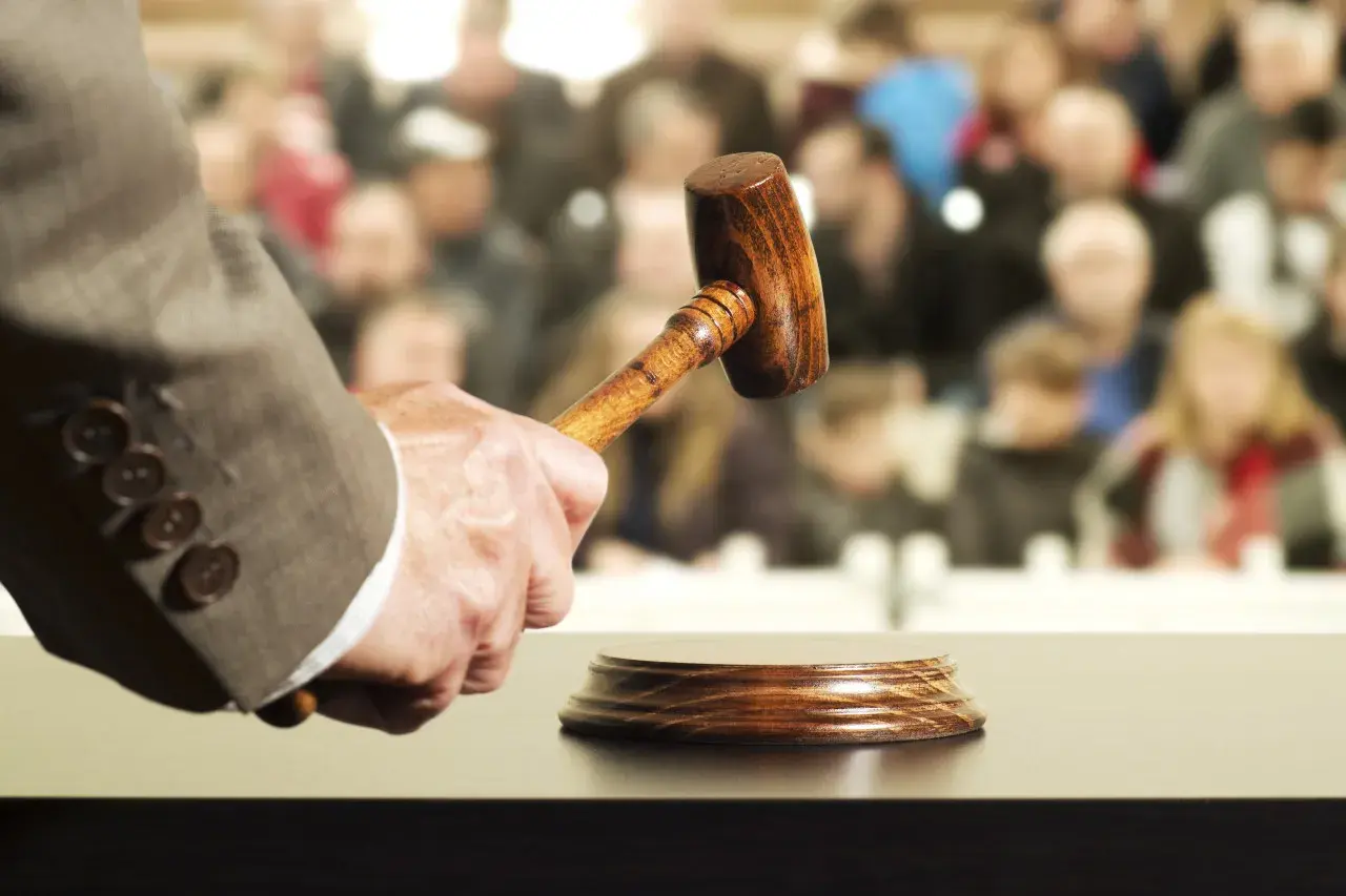 Un commissaire-priseur tient un maillet, prêt à frapper le bloc. La foule attend, espérant acquérir un objet convoité, peut-être au-delà du prix de réserve enchère.