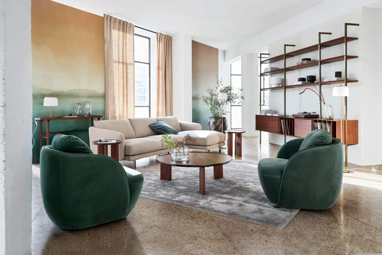 Salon moderne avec canapé beige, fauteuils verts et étagères en bois, ambiance mid century.