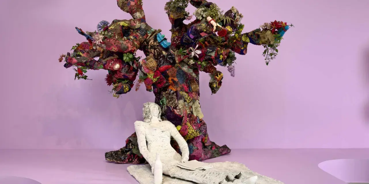 Sculpture d'arbre colorée et texturée, évoquant l'esprit de Niki de Saint Phalle. Une figure blanche repose à ses pieds.