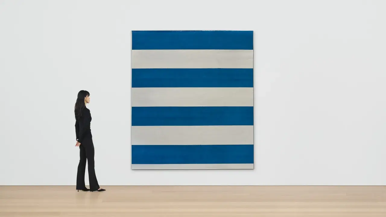 Une femme observe une œuvre de Michel Parmentier, une grande toile rayée de bleu et de blanc, dans une galerie d'art.
