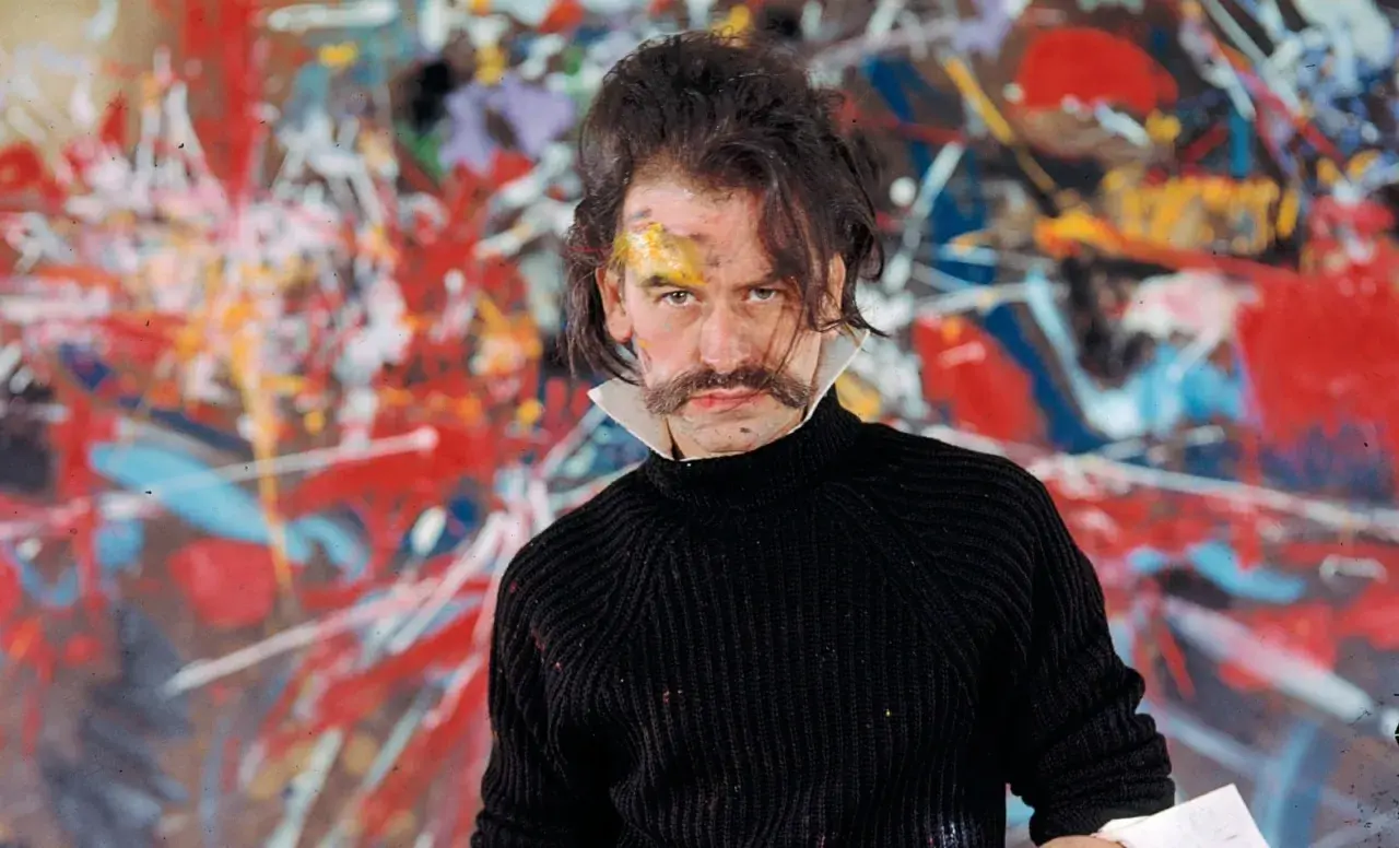 Georges Mathieu, lauréat du prix, pose devant une toile abstraite vibrante, son visage marqué par la peinture.