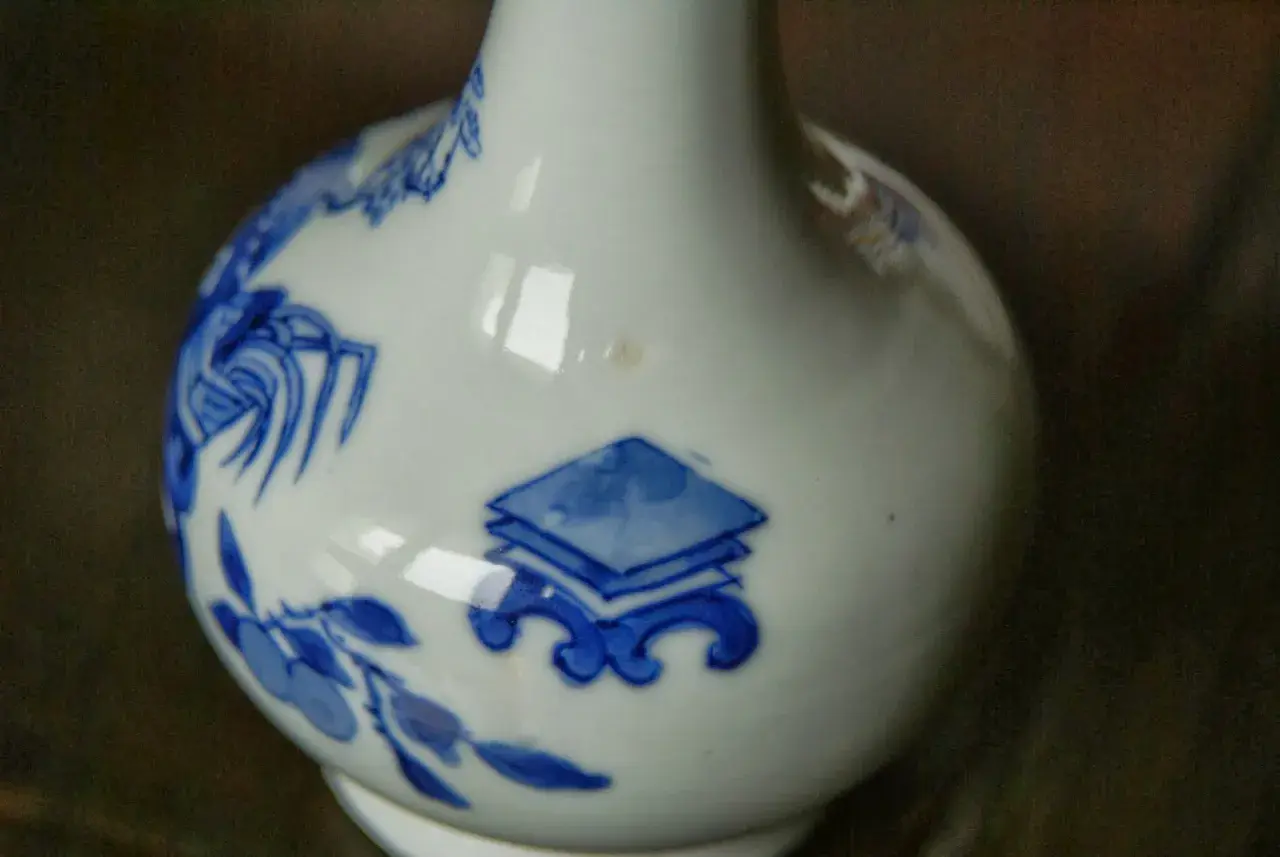 Gros plan sur un vase chinois ancien, blanc avec des motifs bleus de fleurs et de symboles.