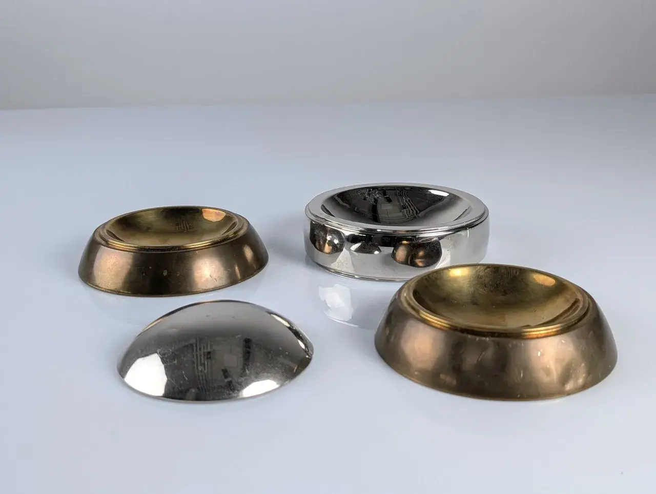 Quatre coupelles en laiton et argent, inspirées par le design de Tommaso Barbi, reflètent la lumière sur leur surface polie.