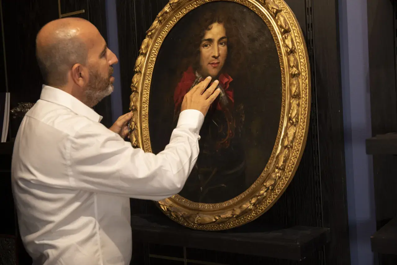 Un homme examine un portrait ancien. Il touche le cadre doré, peut-être pour comment estimer un tableau avec signature.