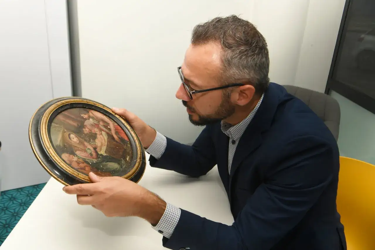 Un homme examine un tableau ancien, cherchant des indices pour savoir comment vendre un tableau.